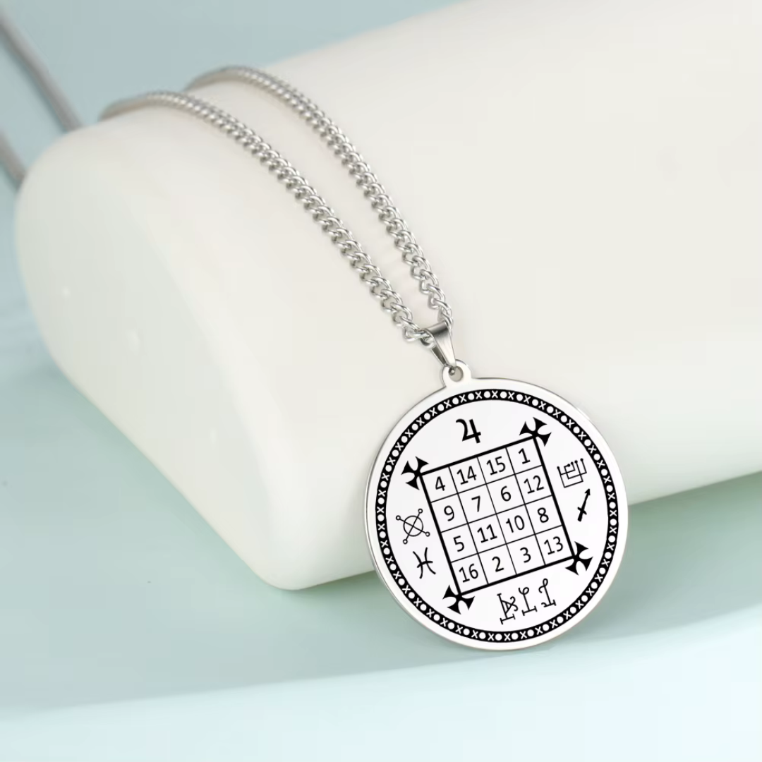 A silver-toned circular pendant necklace with a black occult-style magic square grid and symbols, displayed on a white curved stand against a pale blue background.
