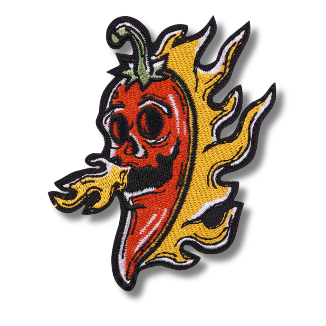 Embroidered patch of a red pepper with black eyes and yellow flames on a white background