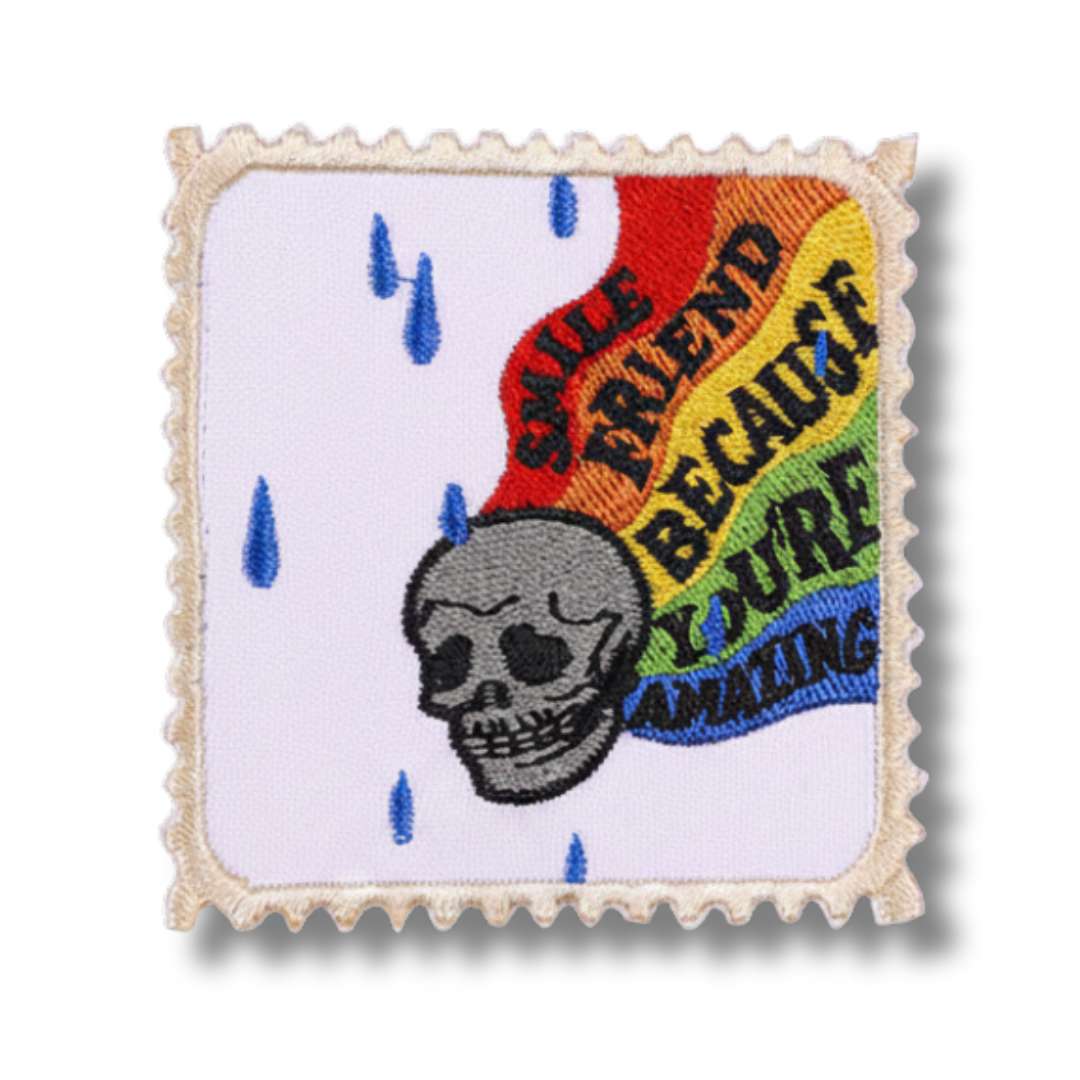 Embroidered patch with a skull design and rainbow-colored text on a white background