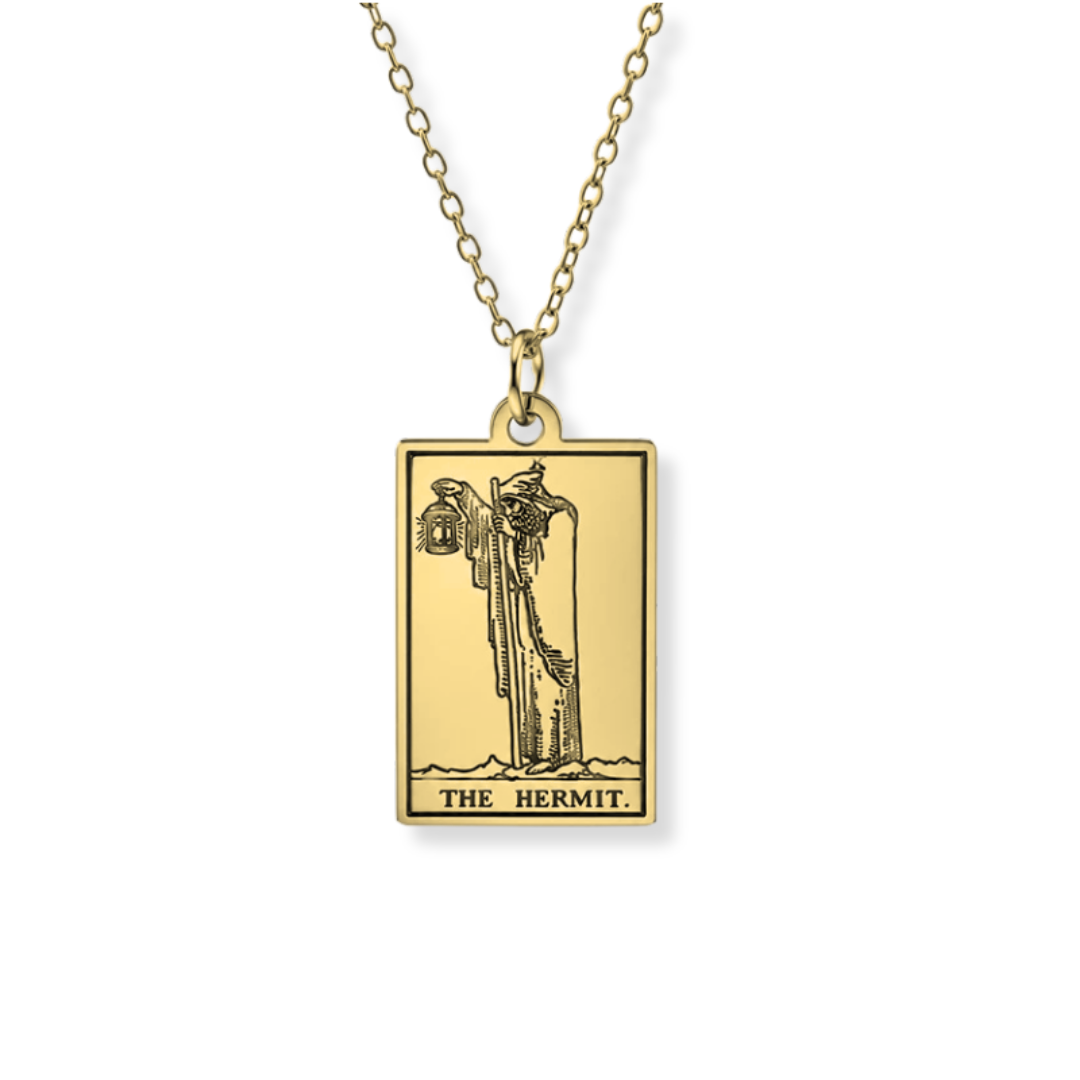 A gold-toned pendant necklace featuring the 'The Hermit' tarot card design, suspended from a matching chain against a plain white background.
