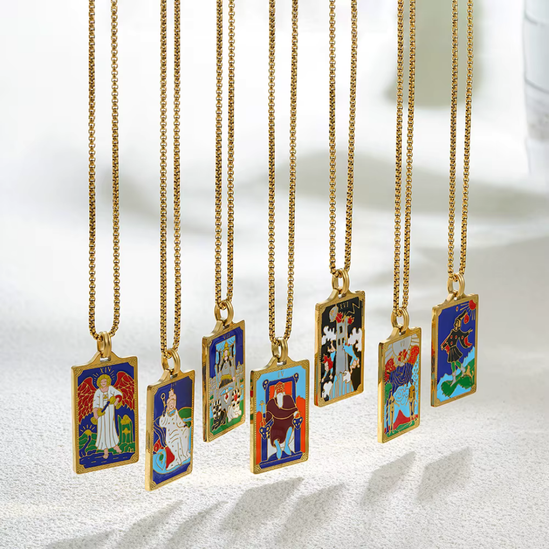 Collection of tarot card-themed pendants on gold chains against a marble 
background