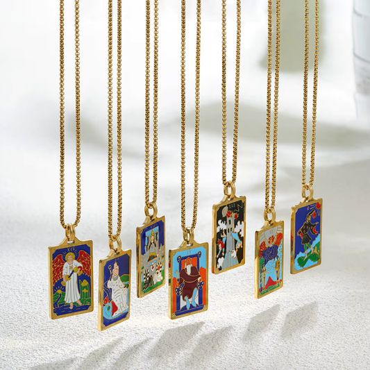 Collection of tarot card-themed pendants on gold chains against a marble 
background
