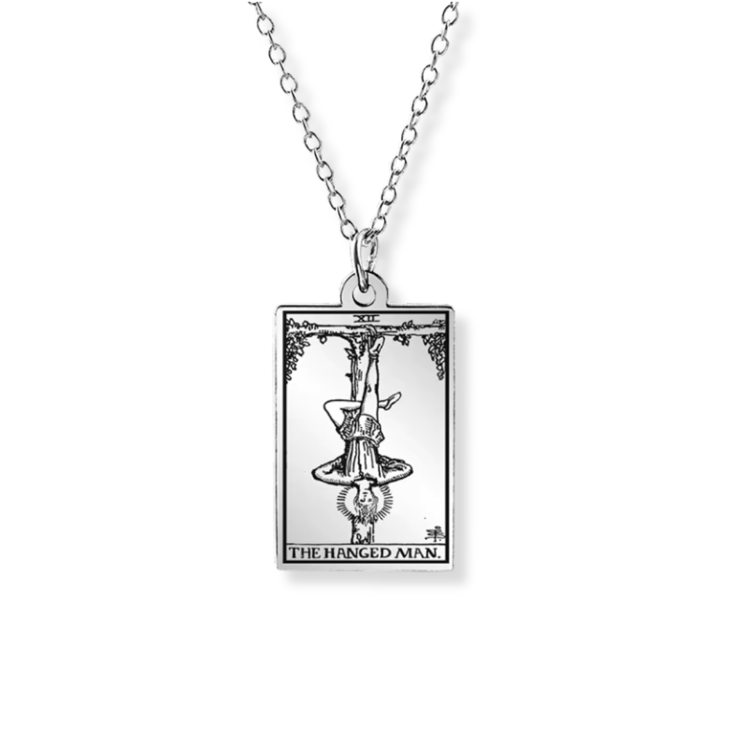A silver-toned necklace featuring a rectangular pendant with an engraved tarot card design labeled 'THE HANGED MAN' on a plain white background.