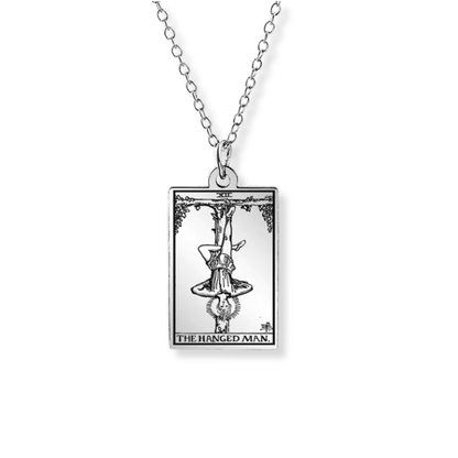 A silver-toned necklace featuring a rectangular pendant with an engraved tarot card design labeled 'THE HANGED MAN' on a plain white background.