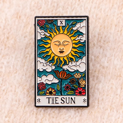 The Sun tarot card enamel pin displayed on beige textured fabric surface showing vibrant colors and intricate vintage design details