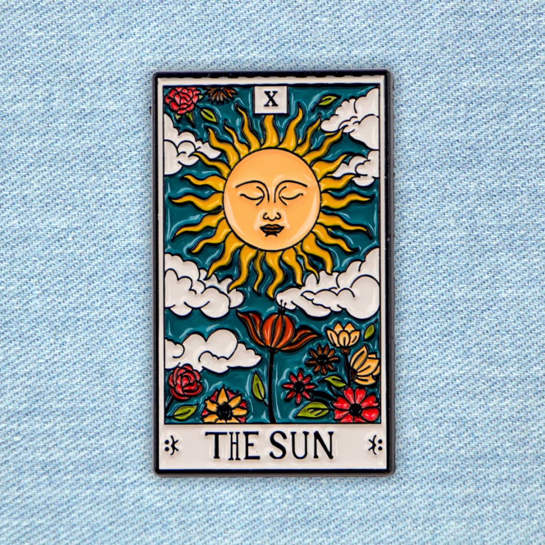 The Sun tarot card enamel pin displayed on light blue denim fabric showing how the pin looks when worn on jeans or denim jacket