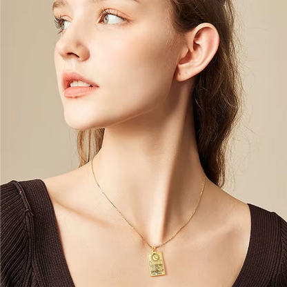 A close-up of a woman wearing a delicate gold chain necklace with a rectangular gold pendant featuring the moon tarot card, set against a soft beige background.