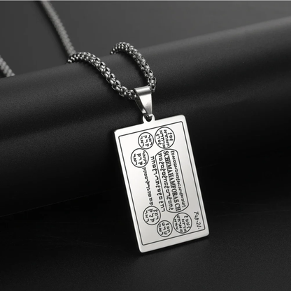 A silver rectangular pendant necklace with engraved script and symbols from the 6th & 7th Books of Moses, hanging from a silver chain against a dark textured background.