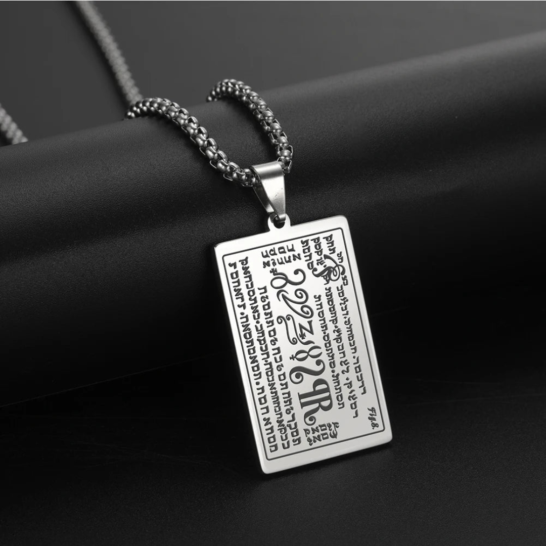A silver rectangular pendant necklace with engraved script and symbols from the 6th & 7th Books of Moses, hanging from a silver chain against a dark textured background.