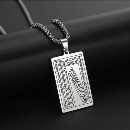 A silver rectangular pendant necklace with engraved script and symbols from the 6th & 7th Books of Moses, hanging from a silver chain against a dark textured background.