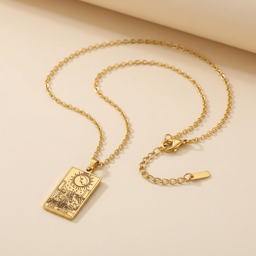 A gold-toned necklace with a rectangular tarot card pendant, displayed on a warm beige background.