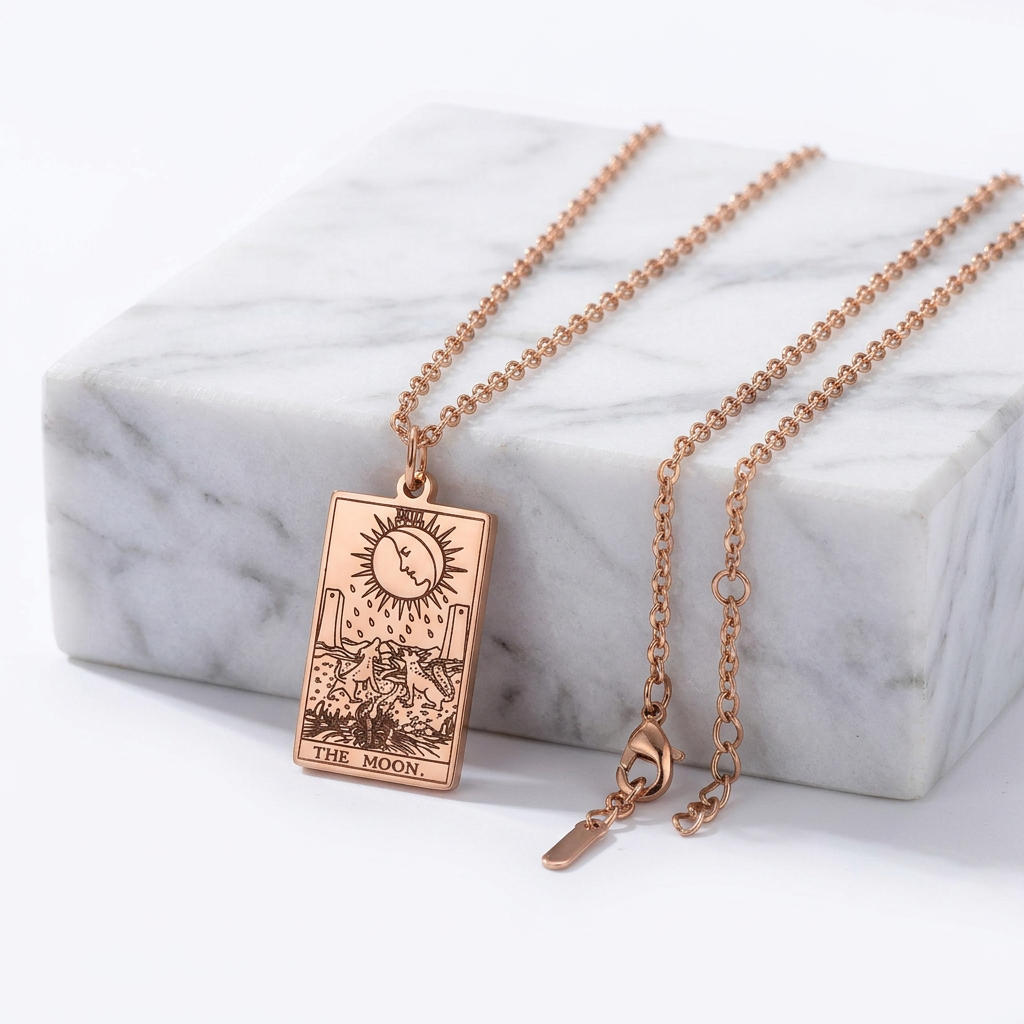 A rose gold tarot card necklace featuring 'The Moon' pendant, displayed on a white marble block against a clean white background.
