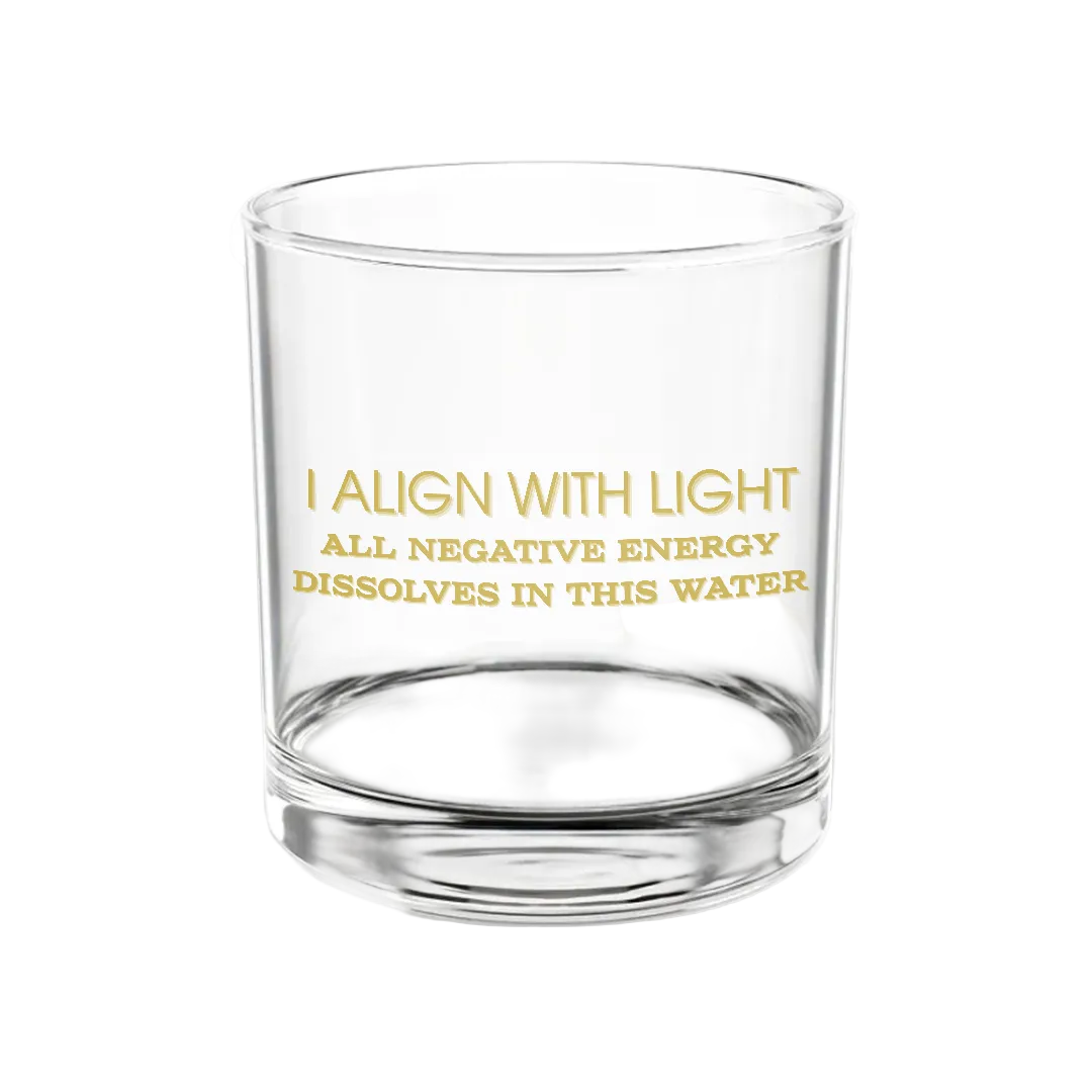 Transparent glass featuring gold script that reads “I align with light | All negative energy dissolves in this water,” set against a plain white backdrop.