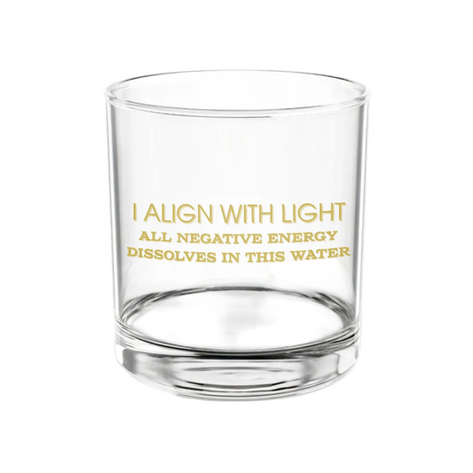 Transparent glass featuring gold script that reads “I align with light | All negative energy dissolves in this water,” set against a plain white backdrop.