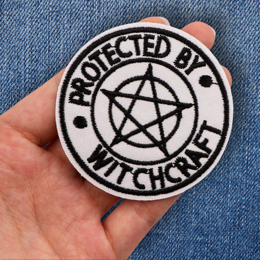 Patch with 'Protected by Witchcraft' text and pentagram symbol held against a denim background.